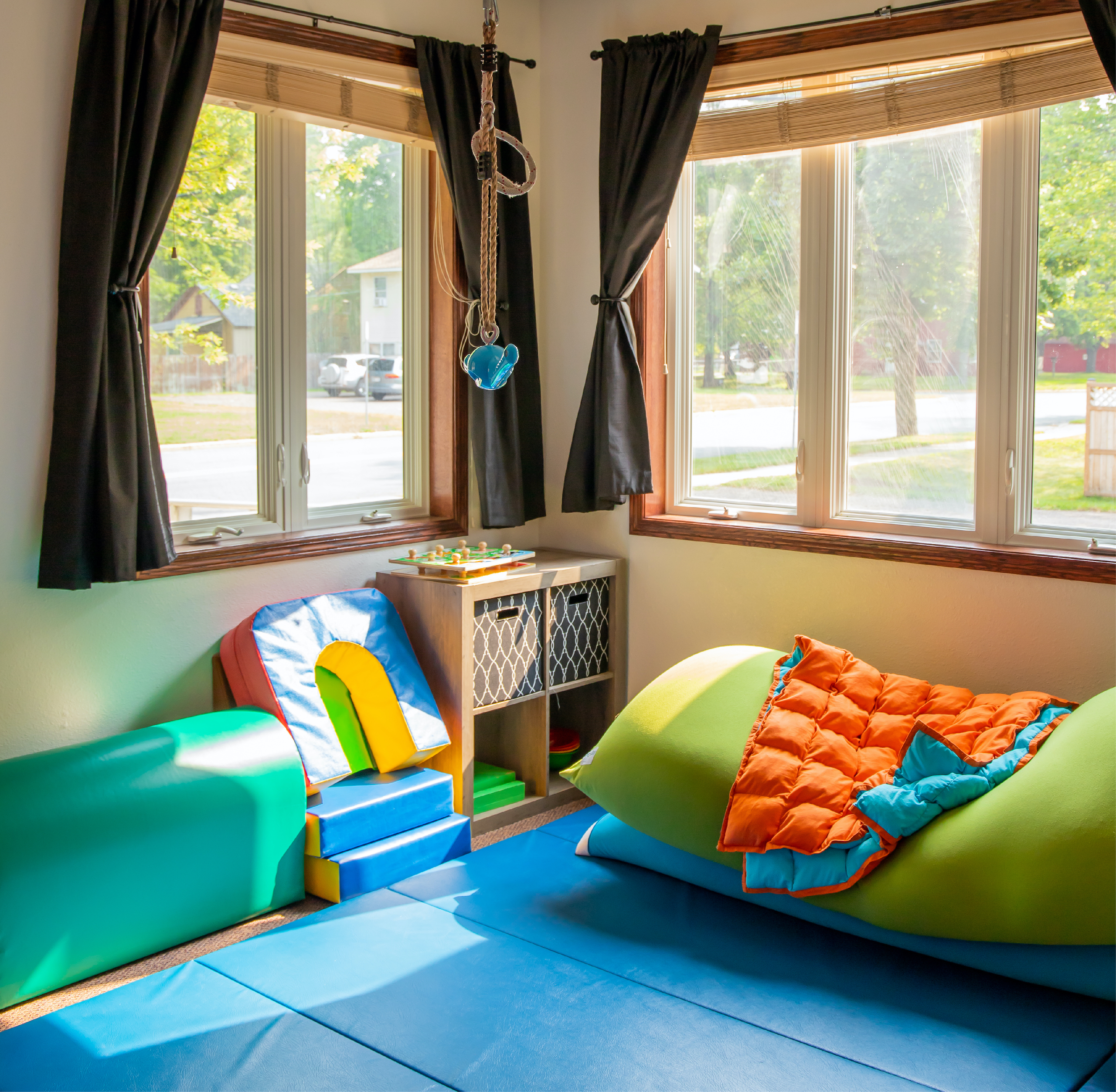 A small room lined with stacked body pillows and cushions with blue floor mats in the middle, all surrounded by windows with sun shining through