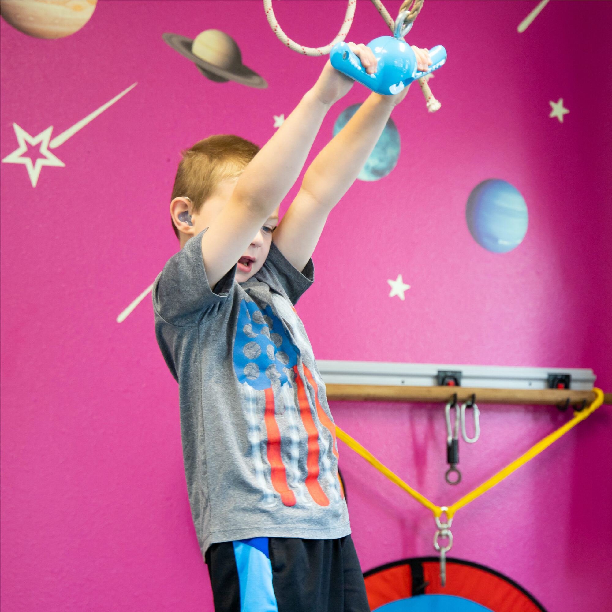 A little boy standing and hanging from a rope with a plastic handle