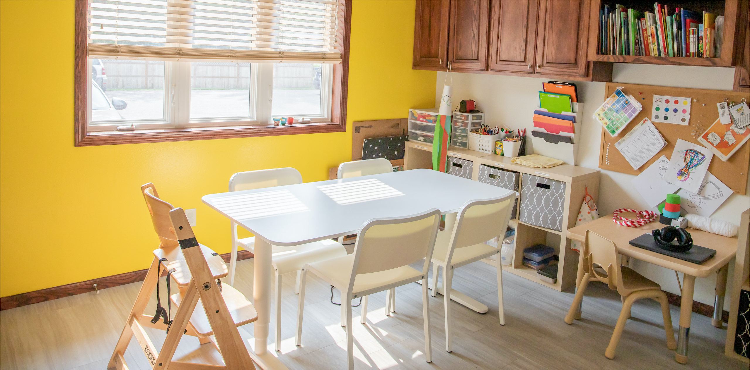 A children's playroom with yellow walls and wood floors with a white table and chairs in the middle of it.