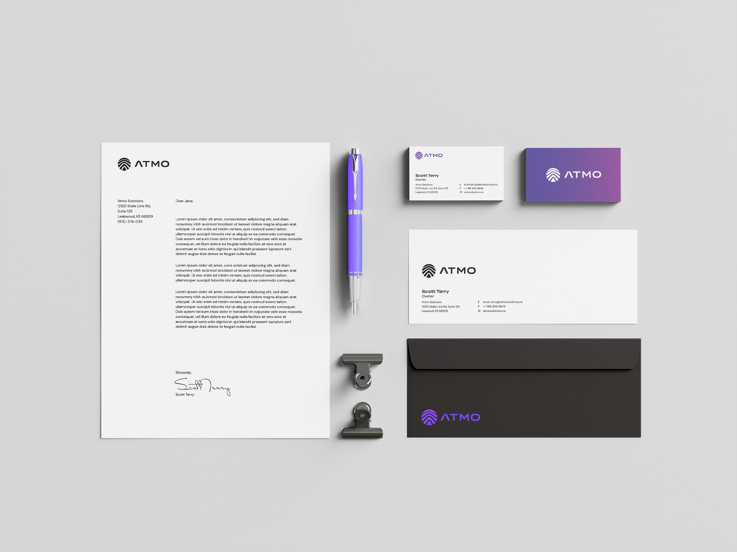 A bird's eye view of brand print collateral including letterhead, a pen, binder clips, business cards, and the front and back of an envelope.