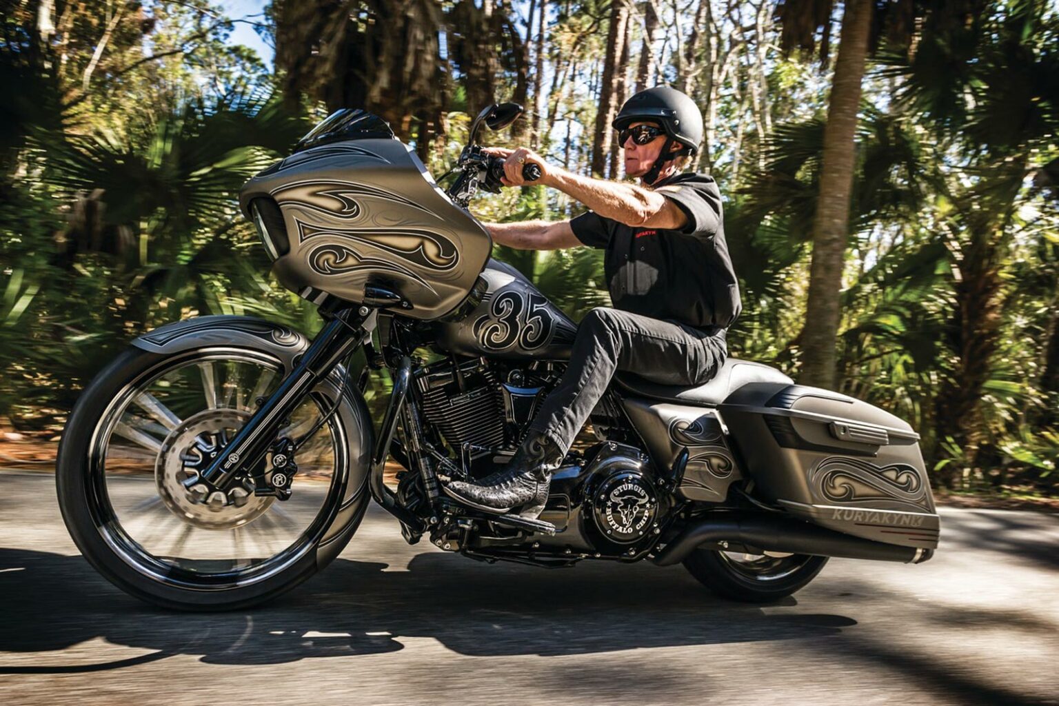 A man wearing black pants, boots, t-shirts, and helmet riding a grey and black motorcycle with decorative swashes on the front.