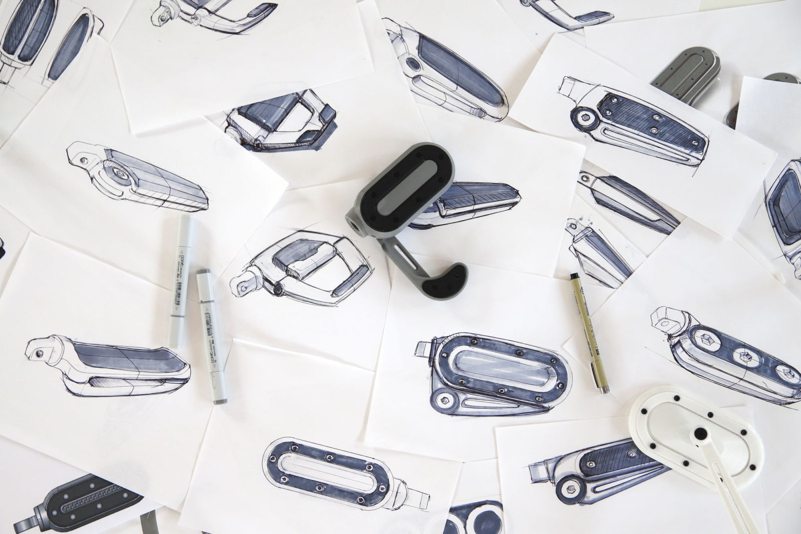 Top down view of a collection of industrial design sketches, the sketches are black and grey on white paper.