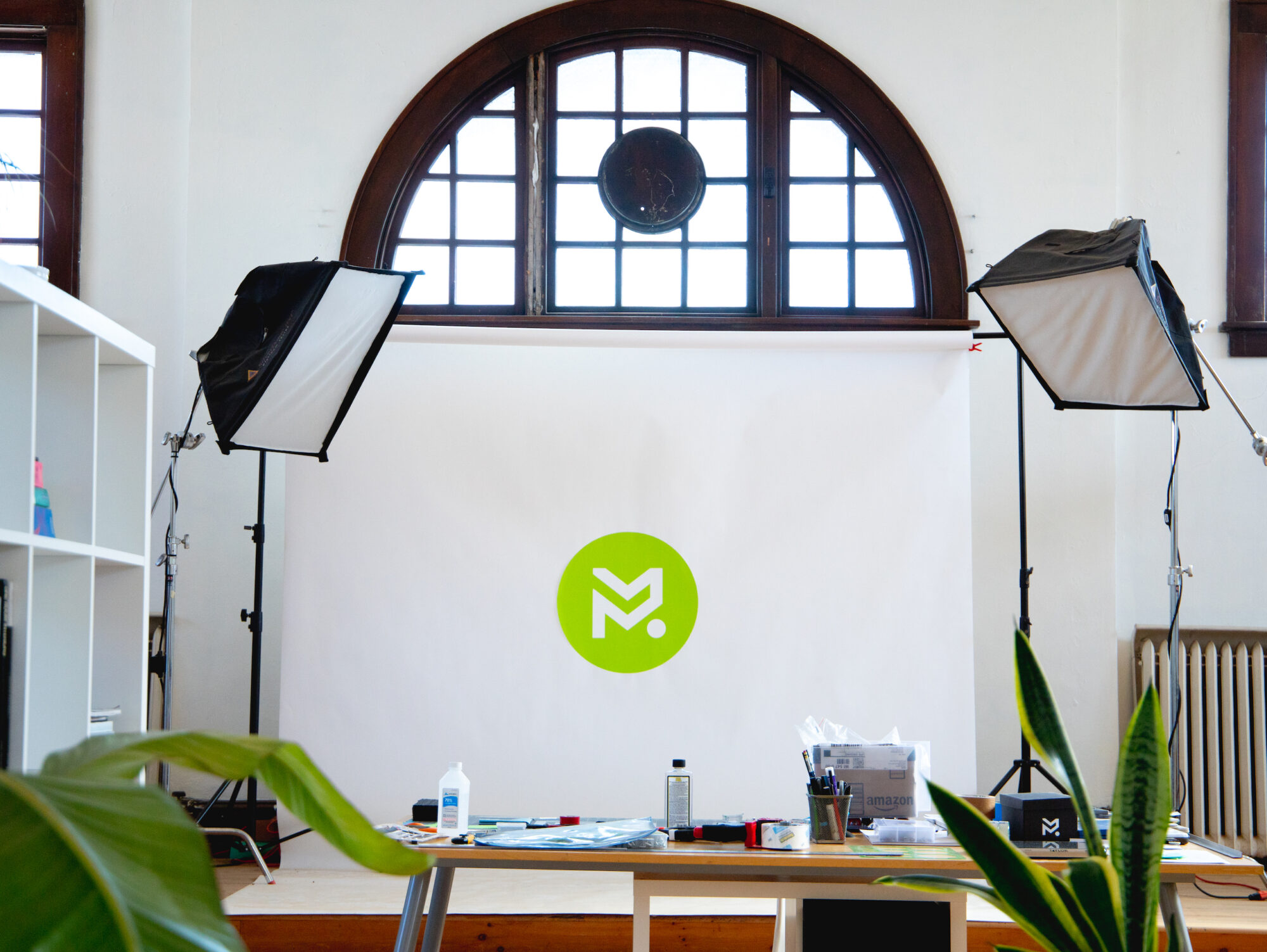 A stage with a whitedrop pulled down over it with photography lights on either side. The Studio MLM logo is mounted in the middle of the background.